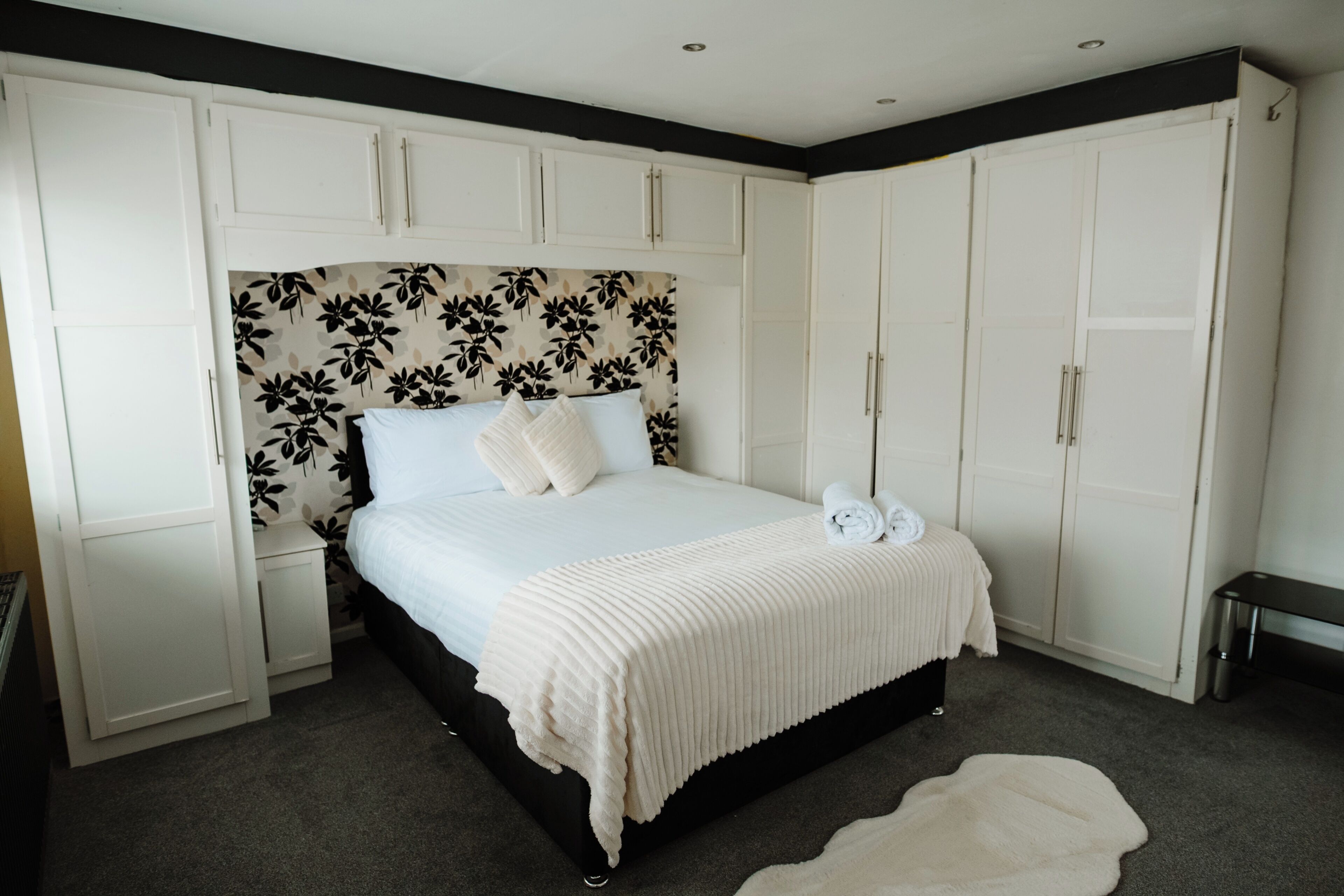 Een slaapkamer met een bed, een witte inbouwkast en een hoofdbord met bloemen.