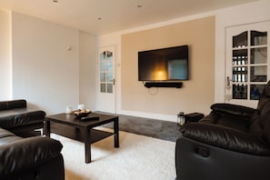 Una sala de estar moderna con un televisor de pantalla plana montado en la pared, una mesa de centro de madera oscura y sofás de cuero negro.