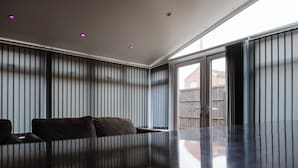 Ein modernes Wohnzimmer mit dunklem, spiegelndem Boden, einem Sofa und vertikalen Jalousien an den Fenstern.
