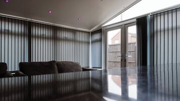 Un salon moderne avec un plancher foncé et réfléchissant, un canapé et des stores verticaux aux fenêtres.