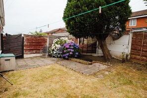 A backyard with a wooden fence, a tree, and a metal chair. - 2 Bed House Sleeps 4 -private Garden -free Parking (Bury)