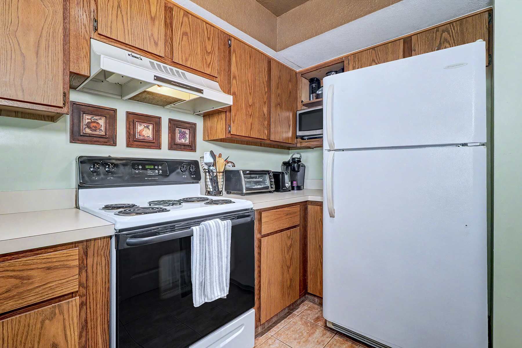 Una cocina con armarios de madera, una estufa blanca, microondas y refrigerador.