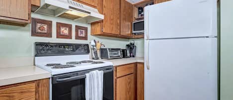 Una cocina con armarios de madera, una estufa blanca, microondas y refrigerador.