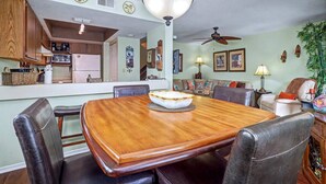 A dining area with a wooden table and chairs, a ceiling fan, and a kitchen in the background. - NEW! Beachfront 2BR + Pool + Walk to Beach (Indian Rocks Beach)