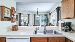A kitchen with a built-in dishwasher, a coffee maker, and a window with curtains. - NEW! Beachfront 2BR + Pool + Walk to Beach (Indian Rocks Beach)
