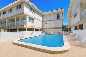 Ein Swimmingpool mit einer 1,8 Meter tiefen Markierung, umgeben von einem weißen Zaun, mit einem Gebäude im Hintergrund, das Balkone und ein Ziegeldach hat.