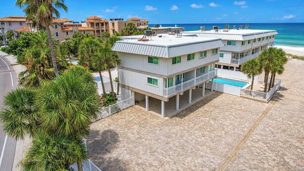 A beachfront hotel with a pool, multiple balconies, and palm trees. - NEW! Beachfront 2BR + Pool + Walk to Beach (Indian Rocks Beach)