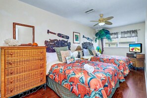 Quarto com cama, cômoda, ventoinha no teto e televisão.