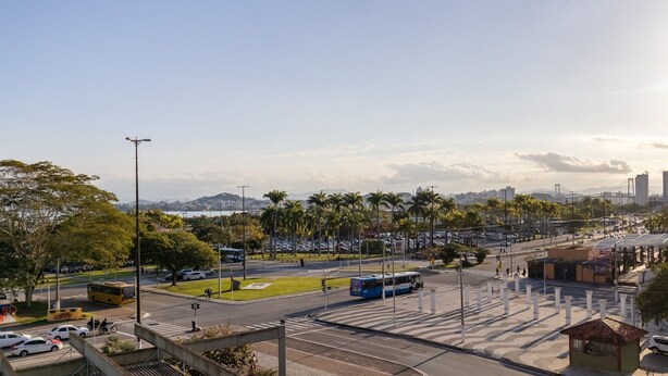 A cityscape with a large parking area, a bus stop, and a bridge in the background. - Fully Equipped apt in Downtown Floripa - Ejo0305 (Florianópolis)