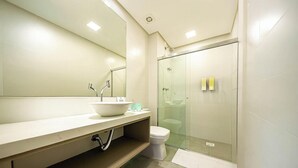 A modern bathroom with a large mirror, a sink, a toilet, and a glass-enclosed shower. - Amazing Studio 5min Walk to the Beach Elu109 (Florianópolis)