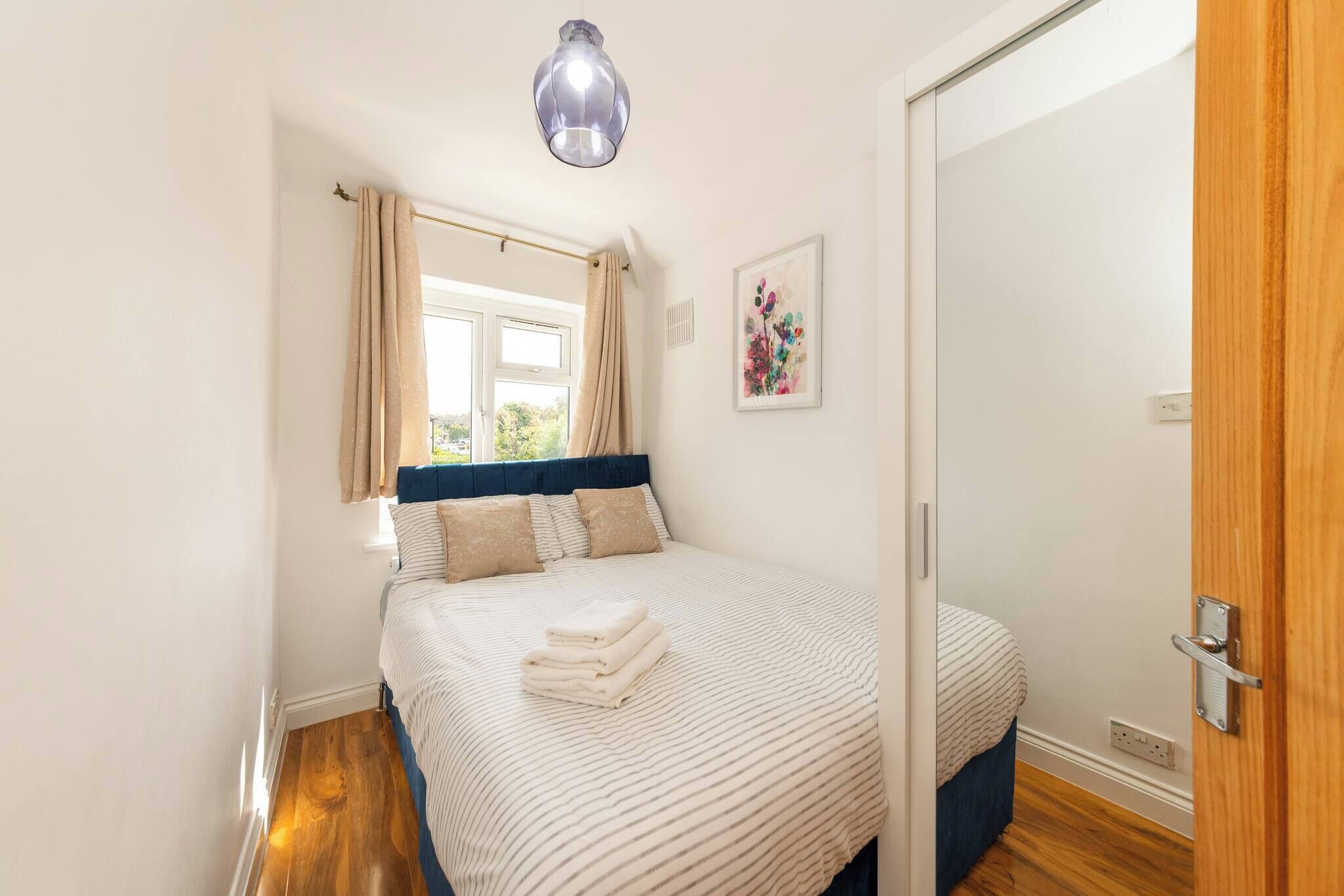 A bedroom with a bed, a window with curtains, a painting on the wall, and a door.