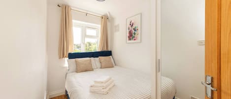 Quarto com cama, janela com cortinas, um quadro na parede e uma porta.