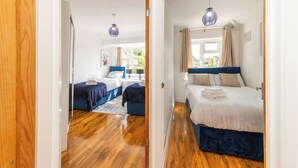 A bedroom with two beds, wooden flooring, and a window with curtains. - Spacious 5-bedroom House in Berkshire - Perfect Family Retreat (Reading)