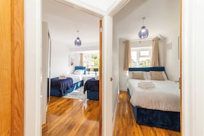 A bedroom with two beds, wooden flooring, and a window with curtains. - Spacious 5-bedroom House in Berkshire - Perfect Family Retreat (Reading)