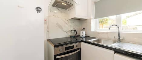 A compact kitchen with white cabinets, a stainless steel sink, a glass kettle, and a built-in oven.