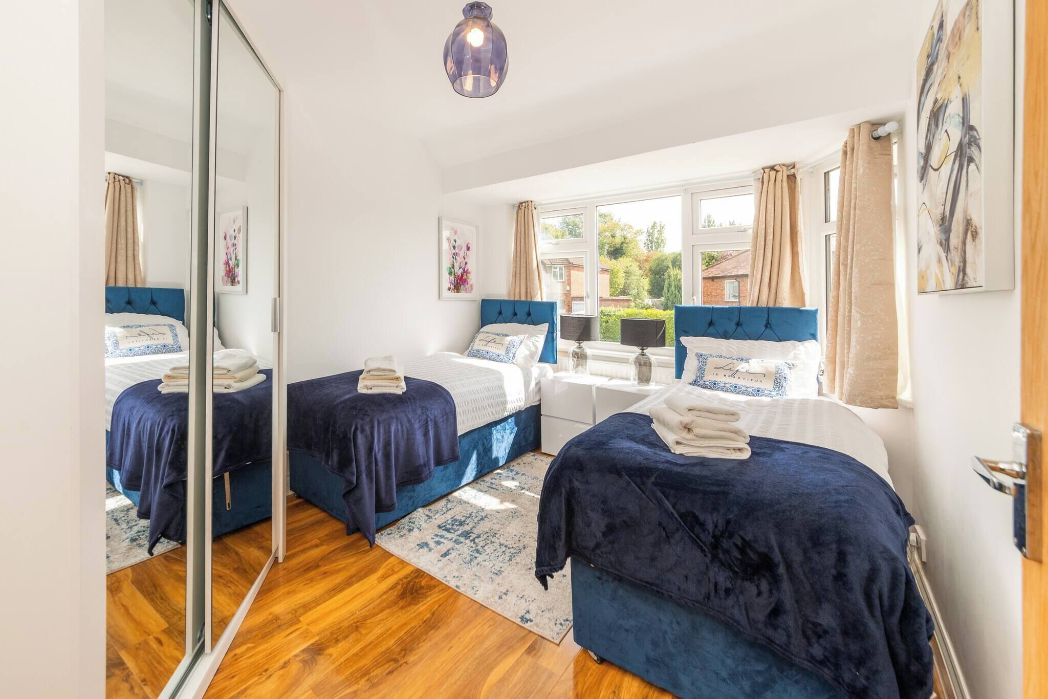 A bedroom with two beds, a mirror, a window with curtains, and a wooden floor.