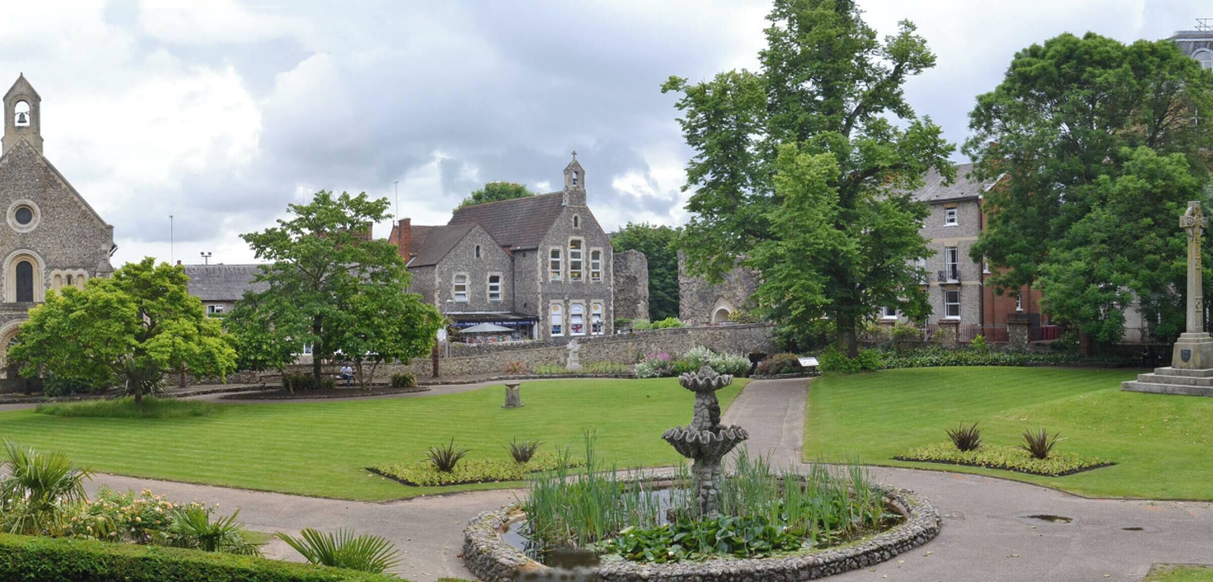 A historic building with a church tower, a fountain, and well-maintained gardens.