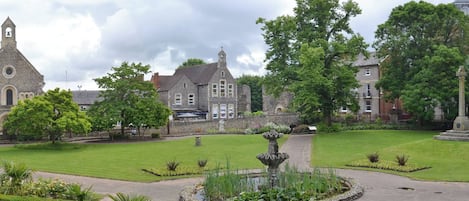 A historic building with a church tower, a fountain, and well-maintained gardens.
