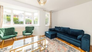 A living room with a green chair, a blue sofa, a glass coffee table, and a patterned rug. - Spacious 5-bedroom House in Berkshire - Perfect Family Retreat (Reading)