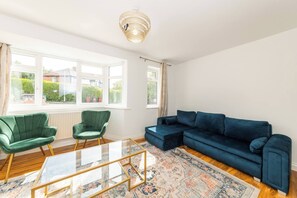 A living room with a green chair, a blue sofa, a glass coffee table, and a patterned rug. - Spacious 5-bedroom House in Berkshire - Perfect Family Retreat (Reading)