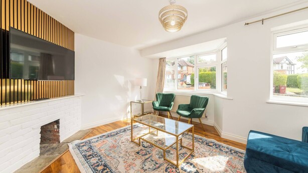A modern living room with a fireplace, a television, a glass coffee table, two green armchairs, and a blue sofa. - Spacious 5-bedroom House in Berkshire - Perfect Family Retreat (Reading)