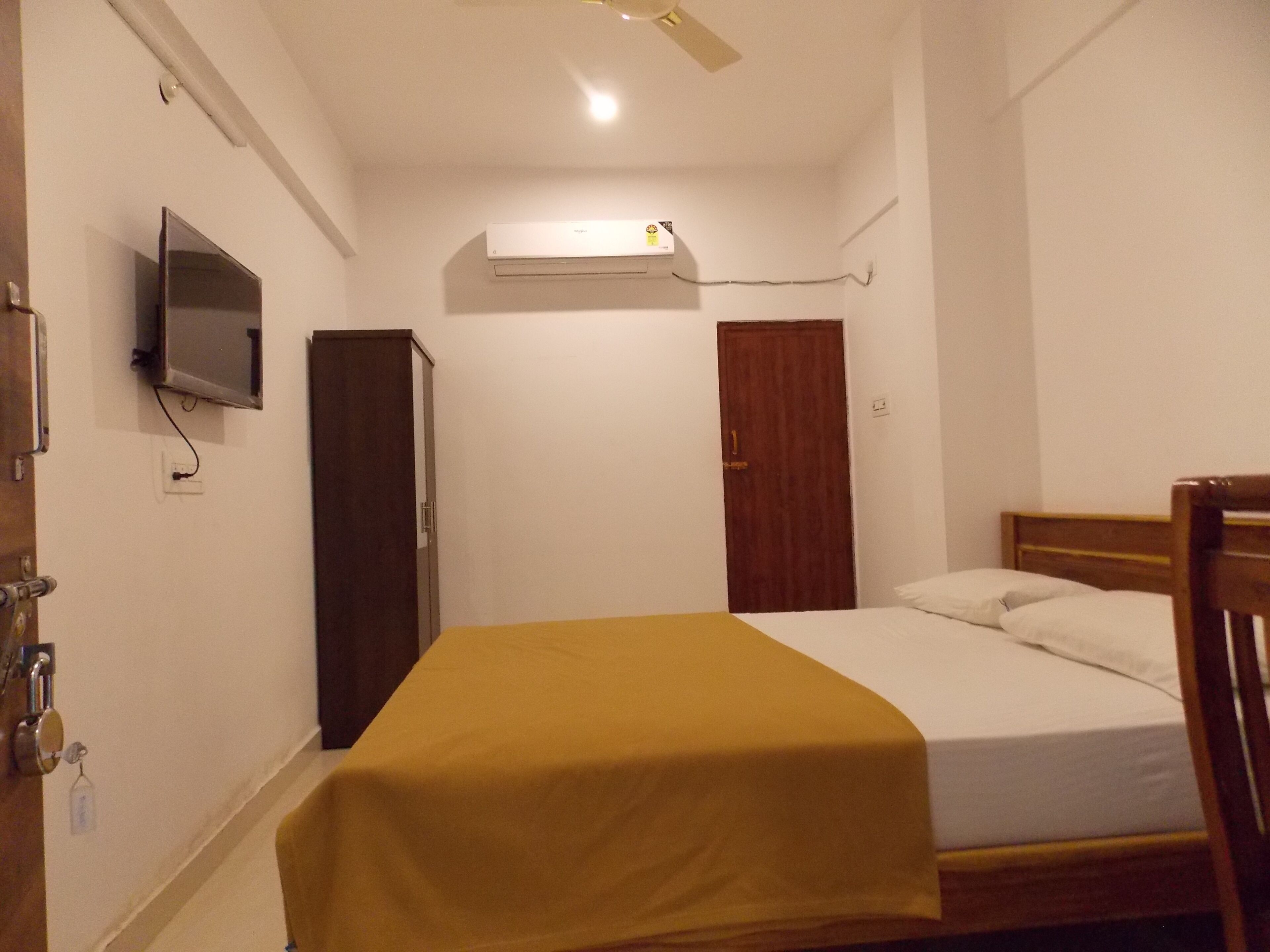 A bedroom with a bed, a television mounted on the wall, an air conditioning unit, and a wooden wardrobe.