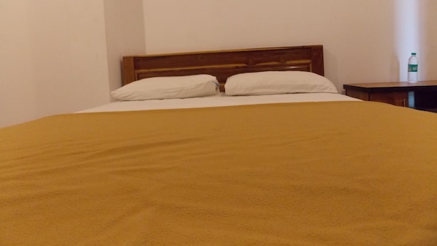 A bed with a wooden headboard, two pillows, and a brown blanket. - SJS Residency by Orange Hotels (Tiruvannamalai)