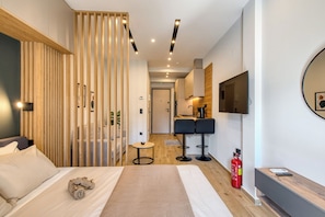 A modern hotel room with a bed, a desk, a chair, a TV, and a fire extinguisher. - Thessaloniki Urban Escape - Studio by ΜΡS (Thessaloniki)