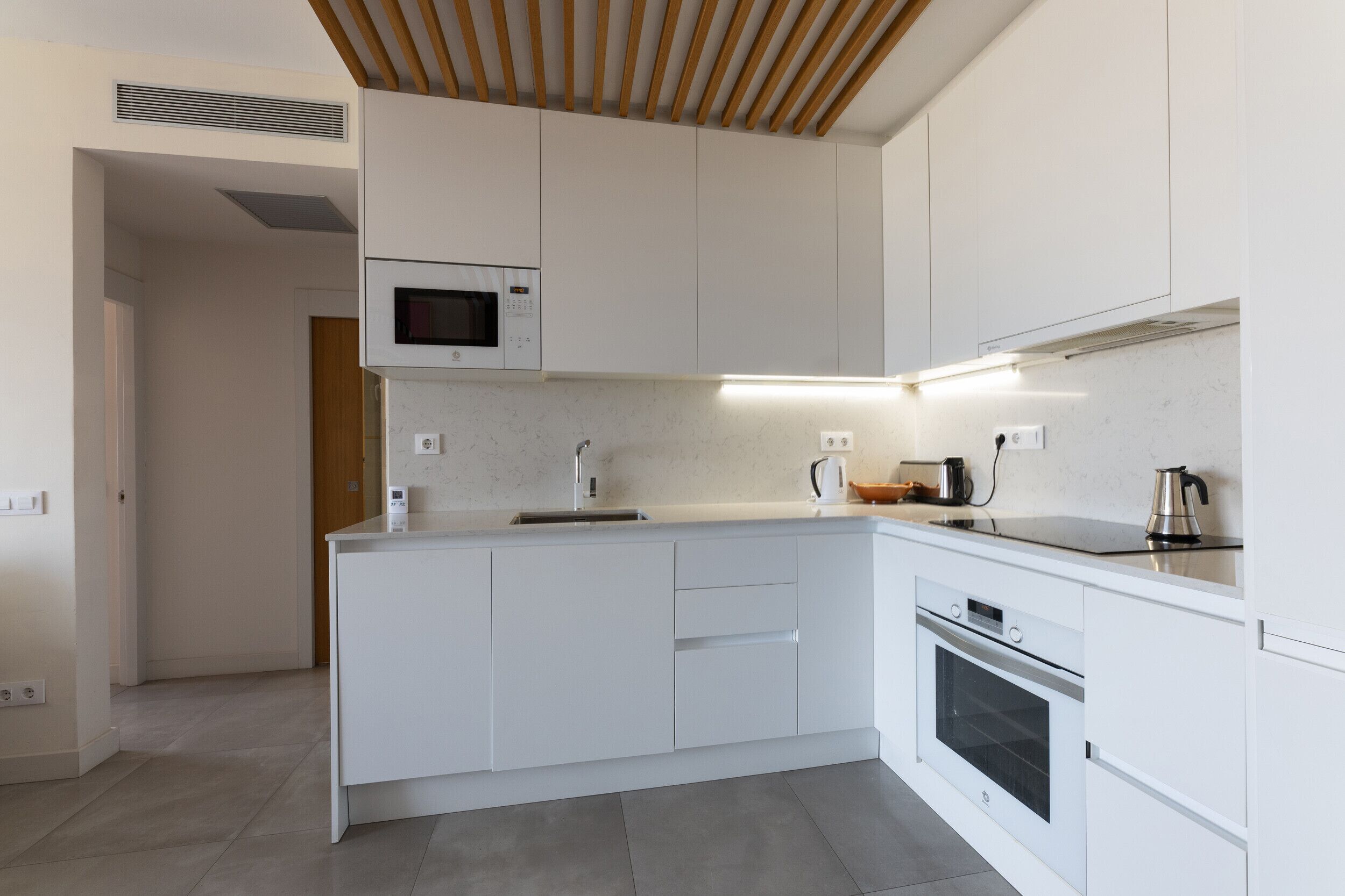 A modern kitchen with white cabinetry, a built-in microwave, a stainless steel kettle, and a dishwasher.