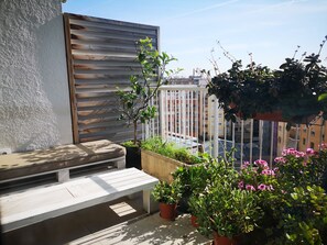 A balcony with a wooden bench, potted plants, and a view of a cityscape. - Atic Deluxe, excellent location (Barcelona)