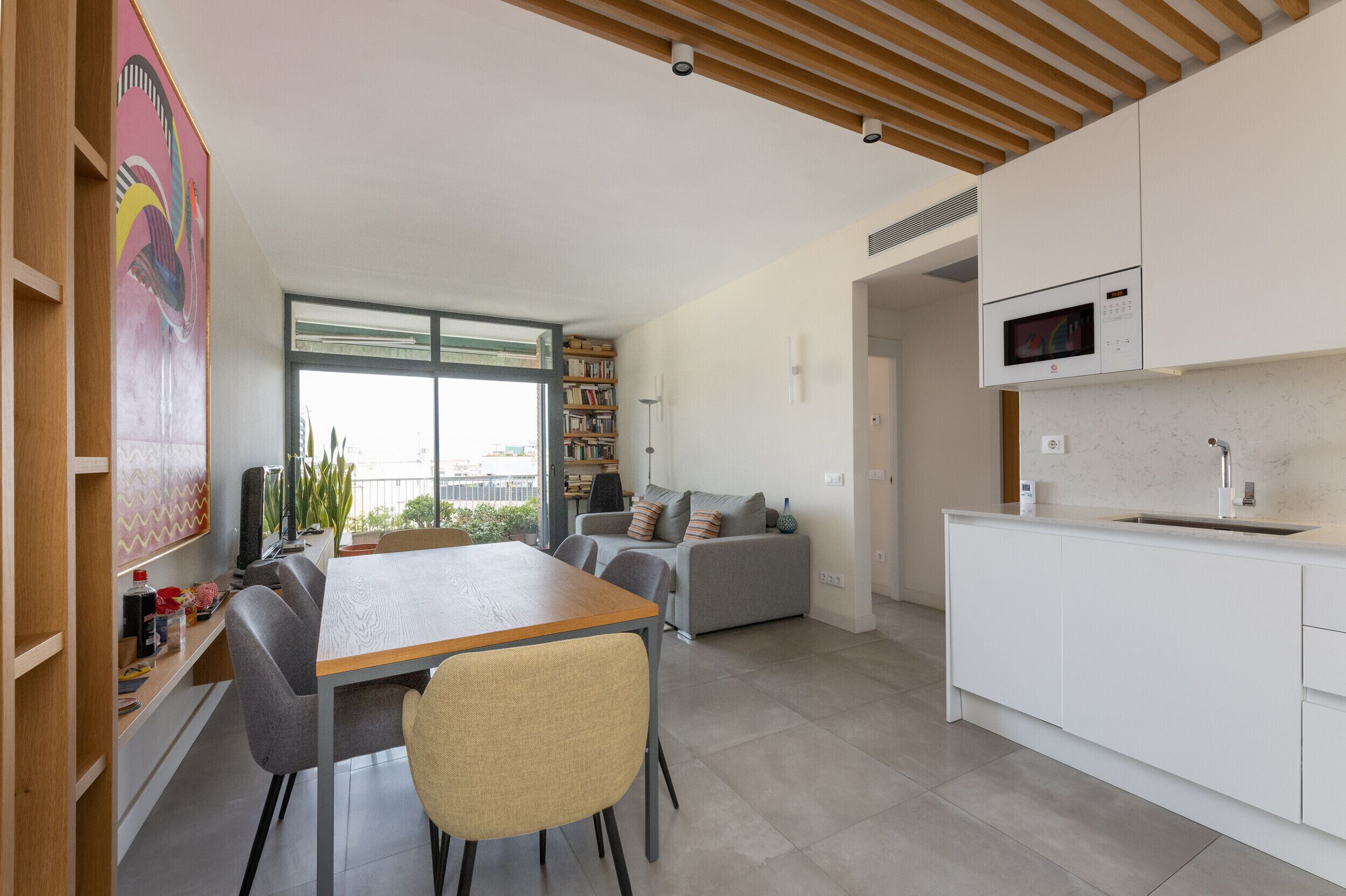 A modern kitchen with white cabinets, a microwave, and a sink. There is a dining area with a table and chairs.