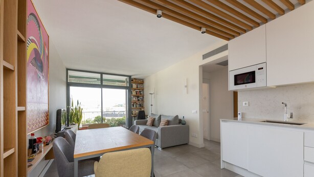 A modern kitchen with white cabinets, a microwave, and a sink. There is a dining area with a table and chairs. - Atic Deluxe, excellent location (Barcelona)