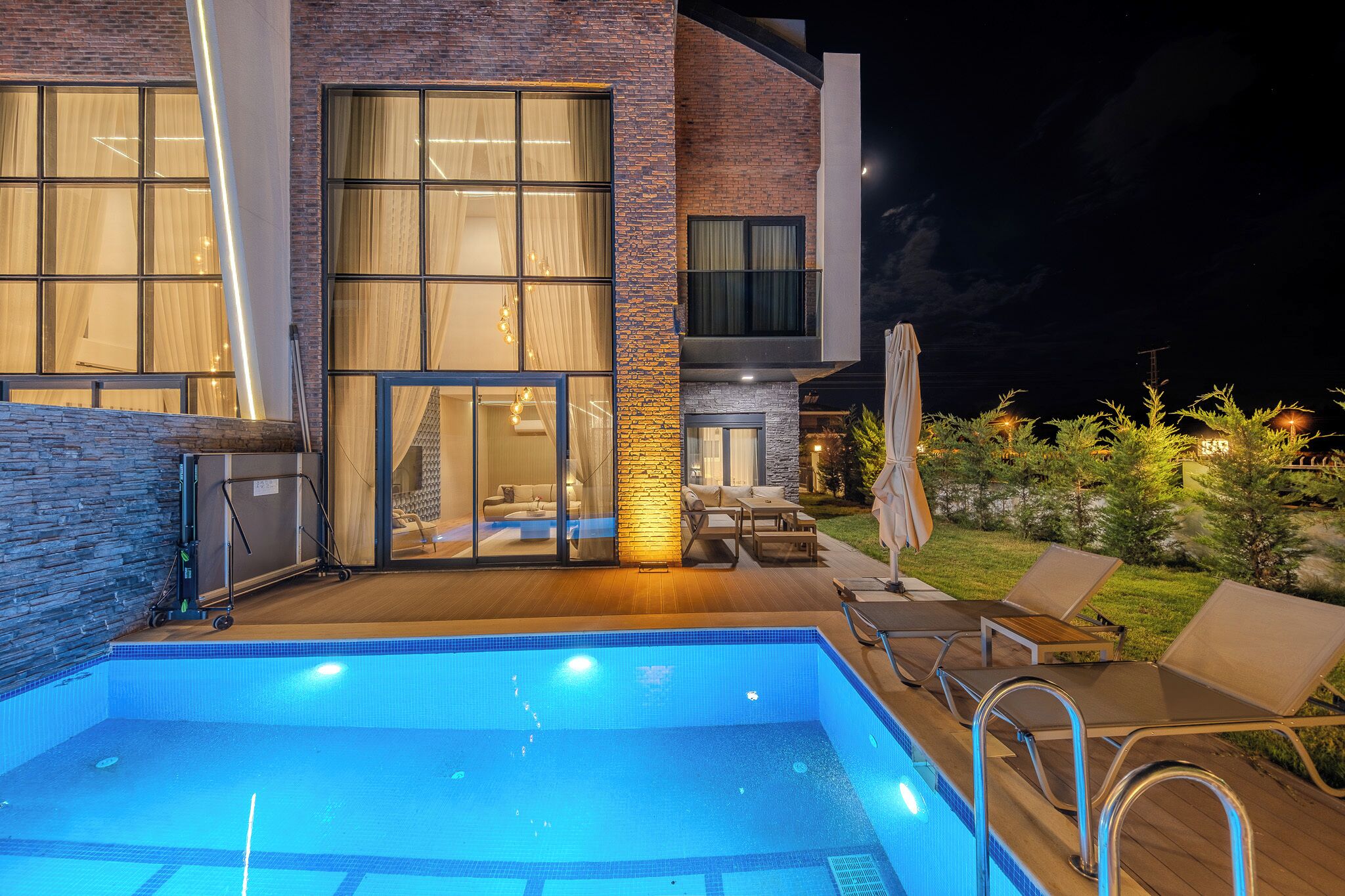 Ein moderner Poolbereich mit Pool, Liegestühlen und einer überdachten Sitzgruppe.
