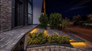 Um edifício moderno com fachada de pedra, entrada bem iluminada e área de jardim ajardinada.