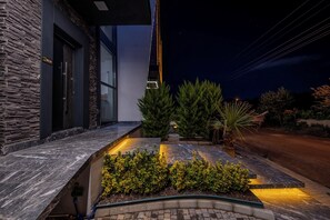 A modern building with a stone facade, a well-lit entrance, and a landscaped garden area.