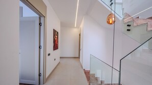 Um interior moderno com escadaria de vidro, um corredor com porta e um quadro na parede.