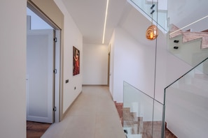 A modern interior with a glass staircase, a hallway with a door, and a painting on the wall.