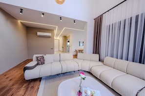 A modern living room with a sectional sofa, a coffee table with a vase, and a dining area in the background. - Luxury Forest Villas with Private Pool in ANTALYA (Antalya)