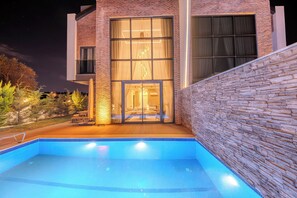 A modern building with a swimming pool, large windows, and a stone wall.