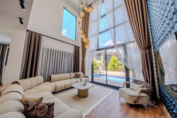 A modern living room with a sectional sofa, a round coffee table, and a view of a swimming pool through large windows.