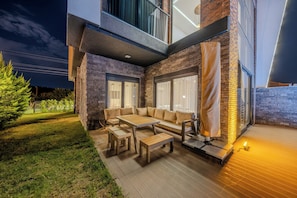 An outdoor seating area with a sofa and tables, a covered bench, and a wooden deck.