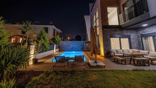 Uma área de piscina moderna ao ar livre com espreguiçadeiras e um muro de pedra.