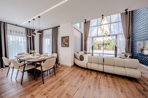 A modern living room with a sofa, dining area with a table set for two, and a large window with curtains.