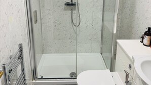Uma casa de banho moderna com cabine de duche em vidro, sanita branca e toucador com lavatório.