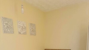 Uma cama de solteiro com cabeceira, uma mesa de cabeceira com abajur, e três obras de arte penduradas na parede.