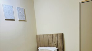 Uma cama de solteiro com cabeceira, mesa de cabeceira e duas obras de arte penduradas na parede.