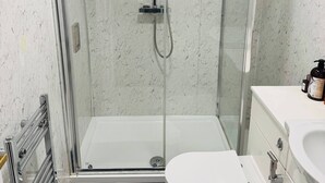 Uma casa de banho moderna com cabine de chuveiro em vidro, sanita branca e lavatório.