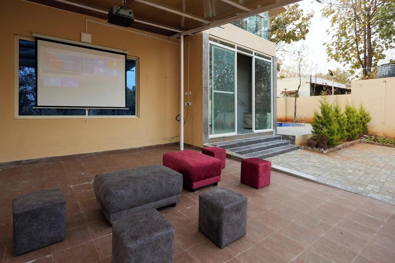An outdoor seating area with a projector screen, a modern building entrance, and a paved patio.