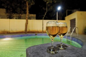 Dois copos de um líquido transparente sobre uma superfície de pedra perto de uma piscina à noite.