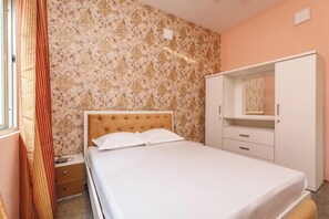 Un dormitorio con cama, armario, mesita de noche y ventana con cortinas.